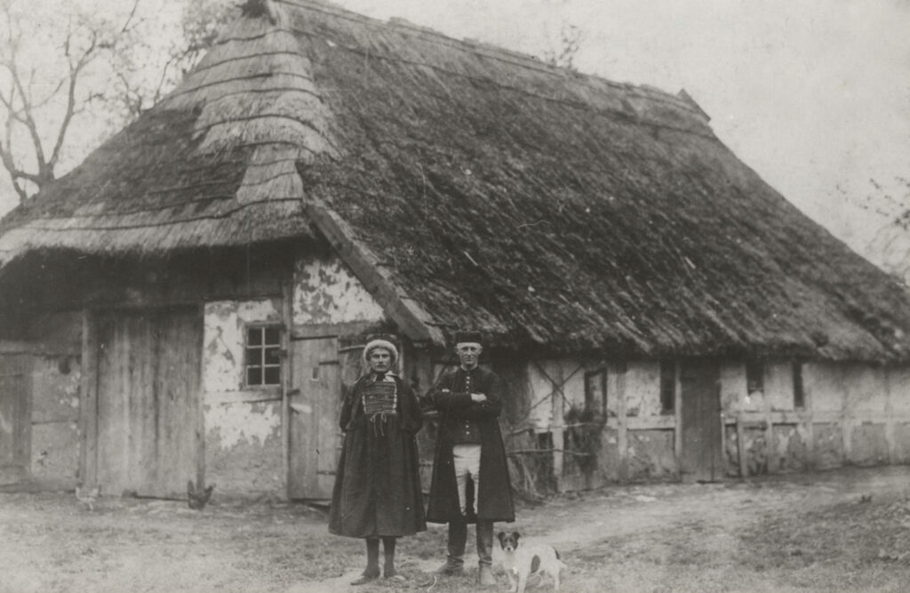 Ostatnia kurna chata w Jamnie, która spłonęła 21 maja 1921 roku. Na pierwszym planie dwójka mężczyzn w strojach jamneńskich - jeden z nich dla żartu ubrał się w strój kobiecy