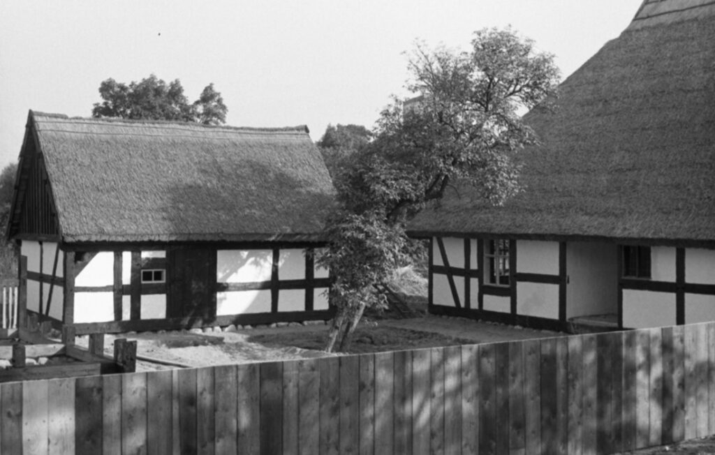 Zabudowania skansenowe z domem o bielonych ścianach i dachu krytym strzechą, teren wokół obiektu w trakcie zagospodarowania (kliknięcie powiększy zdjęcie)