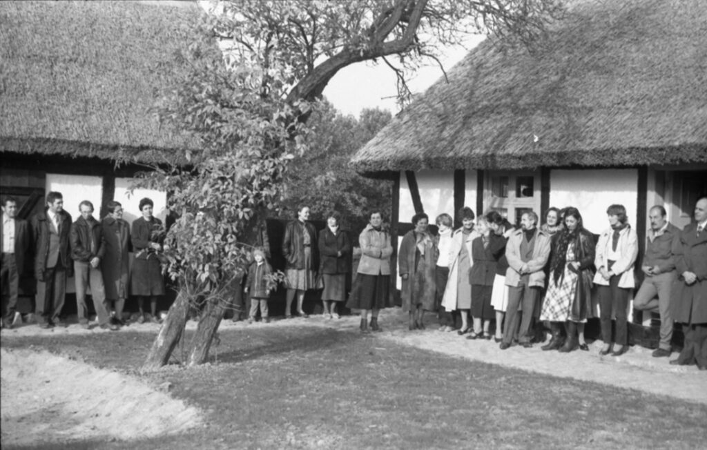 Uczestnicy uroczystości zgromadzeni na dziedzińcu skansenu pomiędzy budynkami o dachach krytych strzechą (kliknięcie powiększy zdjęcie)