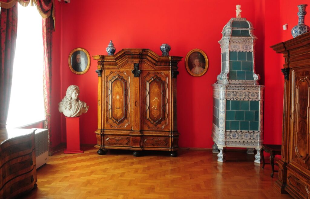 Pokój z drewnianą szafą, piecem kaflowym po prawej i kilkoma portretami na czerwonej ścianie (kliknięcie powiększy zdjęcie)