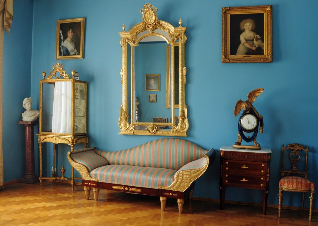 Salon w stylu historycznym z niebieskimi ścianami: sofa w paski, duże złocone lustro, obrazy i komoda z zegarem (kliknięcie powiększy zdjęcie)