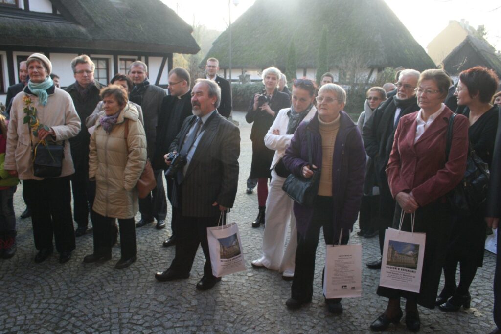 Zgromadzeni goście stojący na dziedzińcu muzeum przed otwarciem wystawy, widok grupy dorosłych uczestników (kliknięcie powiększy zdjęcie)