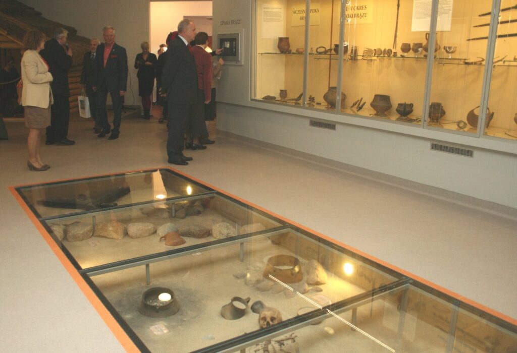 Wnętrze sali wystawowej z gablotami ściennymi i podłogowymi, goście rozpoczynający zwiedzanie ekspozycji (kliknięcie powiększy zdjęcie)