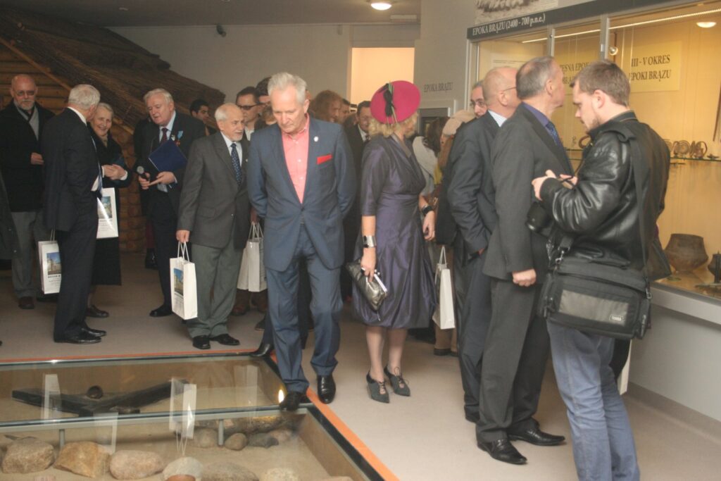 Goście stojący przy przeszklonej gablocie podłogowej z eksponatami, rozmowy podczas zwiedzania wystawy (kliknięcie powiększy zdjęcie)