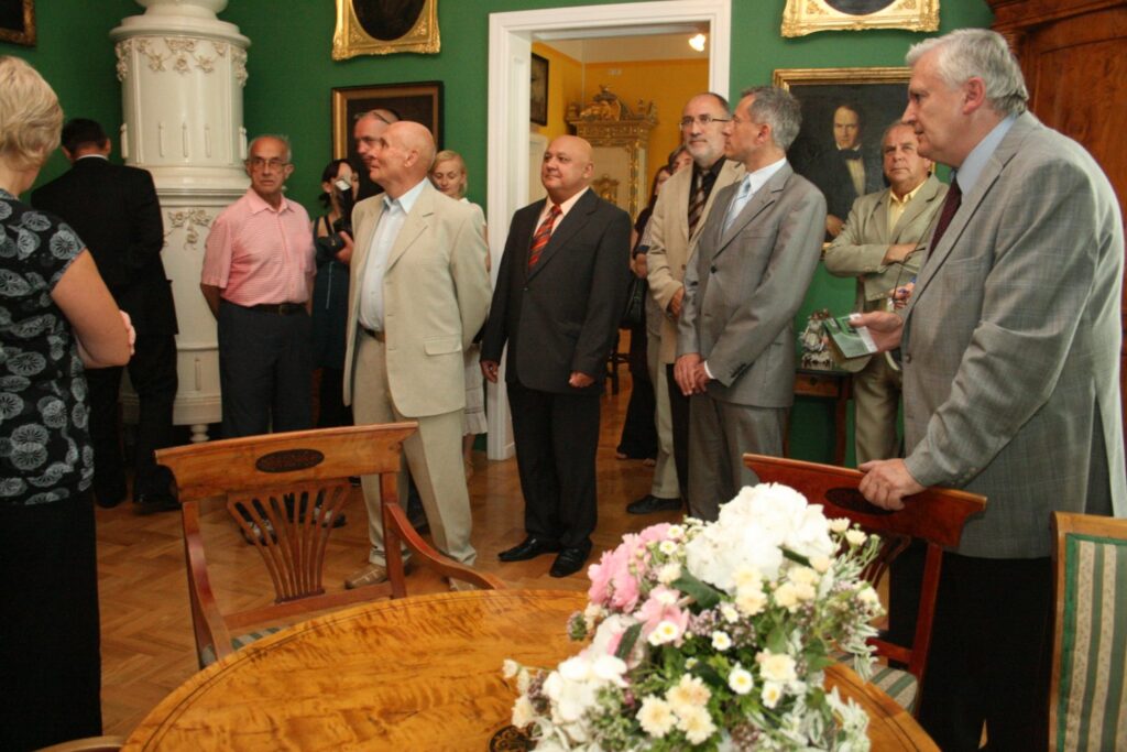 Grupa osób stojących w muzealnej sali z zielonymi ścianami i zabytkowymi meblami, podczas otwarcia wystawy (kliknięcie powiększy zdjęcie)