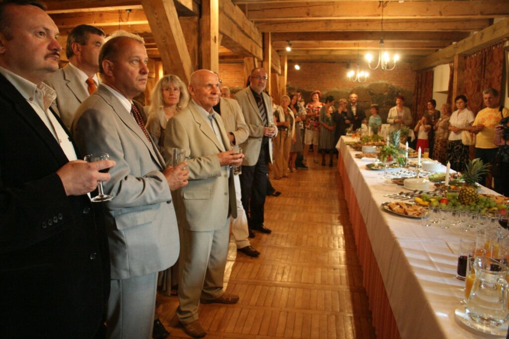 Grupa osób stojących przy długim stole z poczęstunkiem w drewnianym wnętrzu podczas wydarzenia (kliknięcie powiększy zdjęcie)