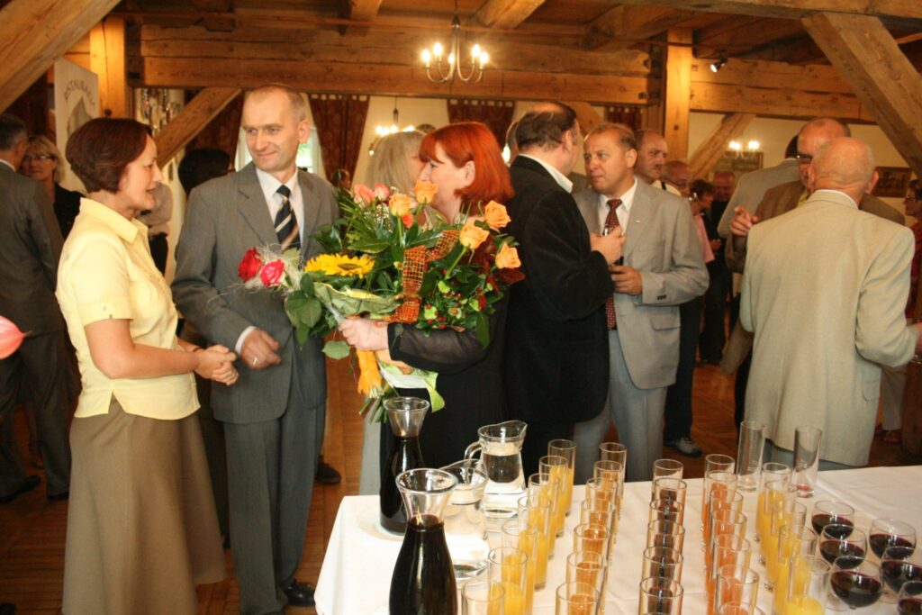 Osoby rozmawiające przy stole z napojami. Jedna z osób trzyma w rękach bukiet kwiatów (kliknięcie powiększy zdjęcie)