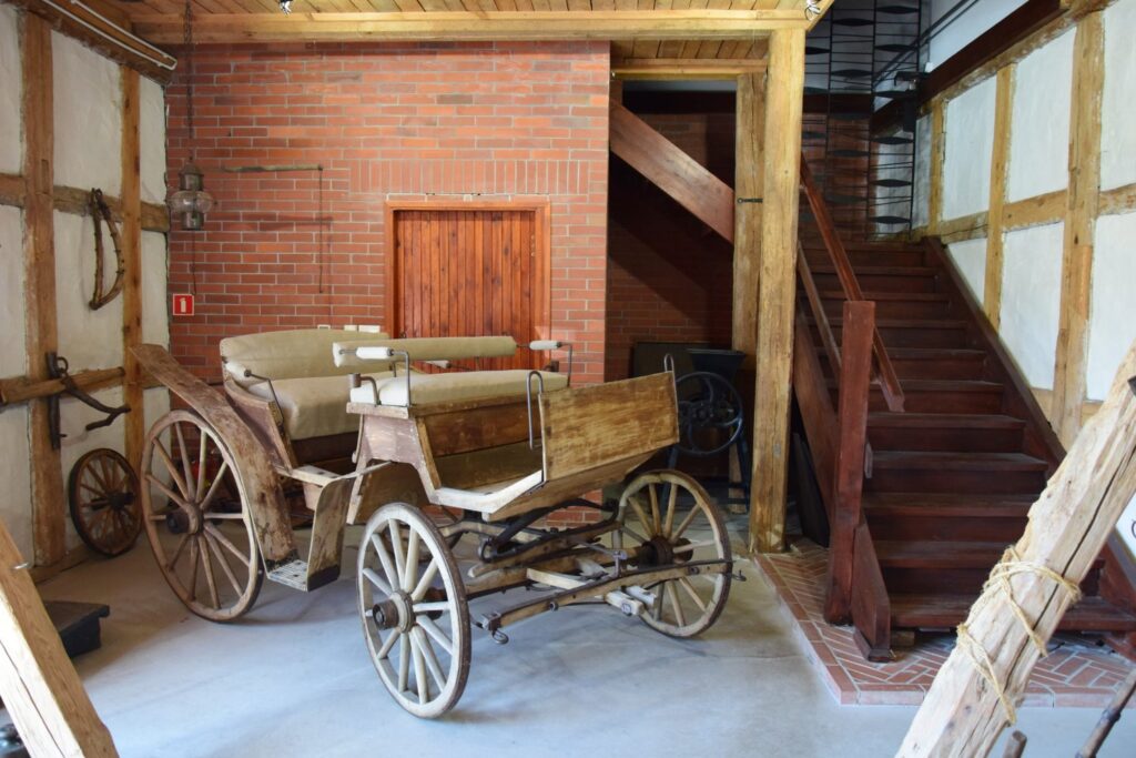 Wnętrze kuźni z drewnianym wozem na kołach, schodami prowadzącymi na piętro oraz elementami wyposażenia warsztatu (kliknięcie powiększy zdjęcie)