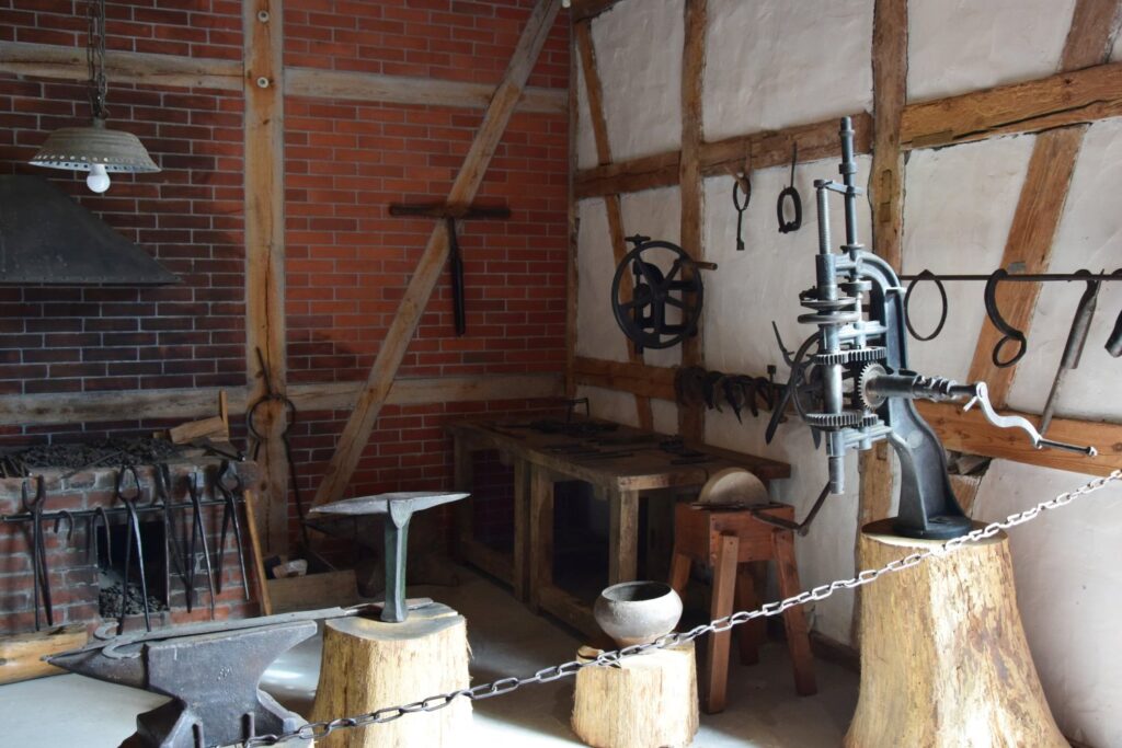 Fragment wnętrza kuźni z kowadłem, imadłem i zestawem narzędzi kowalskich zawieszonych na ścianie (kliknięcie powiększy zdjęcie)