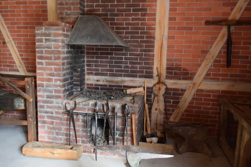 Ceglane palenisko kowalskie z okapem i narzędziami do obróbki metalu ułożonymi przy ścianie (kliknięcie powiększy zdjęcie)