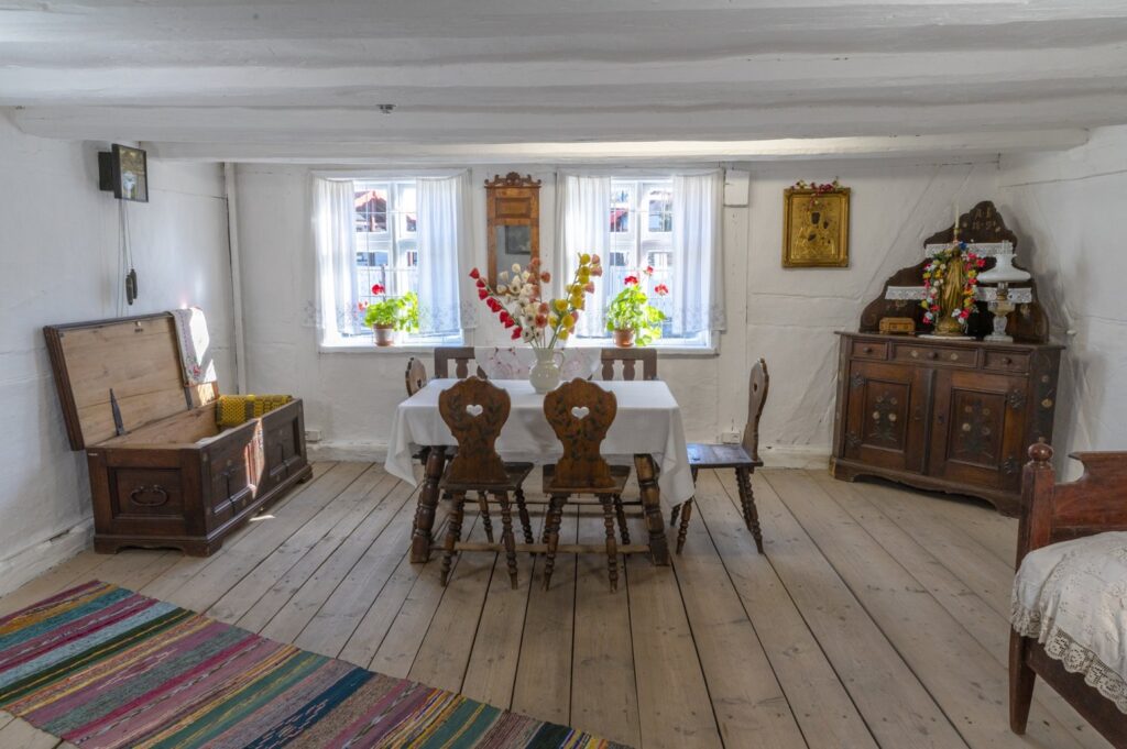 Izba mieszkalna w chałupie – stół z krzesłami, skrzynia, kredens oraz dekoracje przy oknach (kliknięcie powiększy zdjęcie).