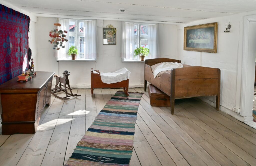 Sypialnia w chałupie – drewniane łóżka, skrzynia, chodniki tkane oraz kołyska ustawiona przy oknie (kliknięcie powiększy zdjęcie).