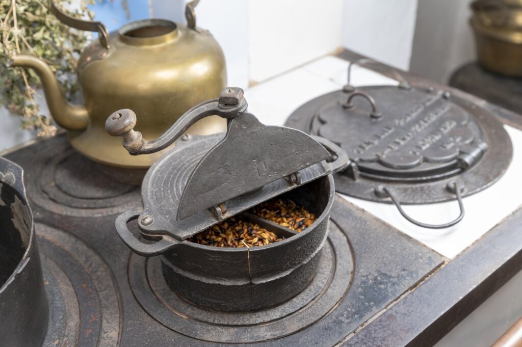 Zbliżenie na piec kuchenny z żeliwnymi pokrywami, czajnikiem oraz młynkiem do mielenia ziaren (kliknięcie powiększy zdjęcie).