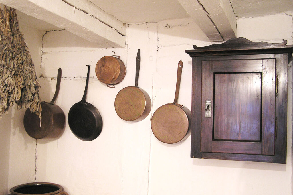 Ściana kuchni z wiszącymi patelniami, deskami do krojenia oraz drewnianą szafką (kliknięcie powiększy zdjęcie).