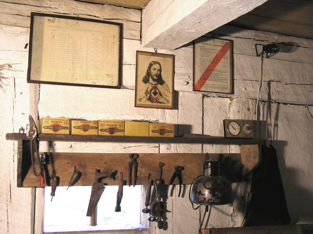 Wnętrze warsztatu szewskiego – półka z narzędziami do obróbki skóry, kopytami szewskimi oraz dokumentami na ścianie (kliknięcie powiększy zdjęcie).