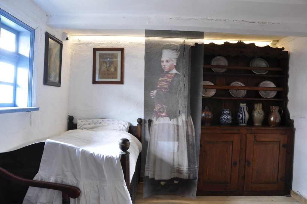 Rekonstrukcja wnętrza izby mieszkalnej z łóżkiem, kredensem i naczyniami; element ekspozycji etnograficznej (kliknięcie powiększy zdjęcie).