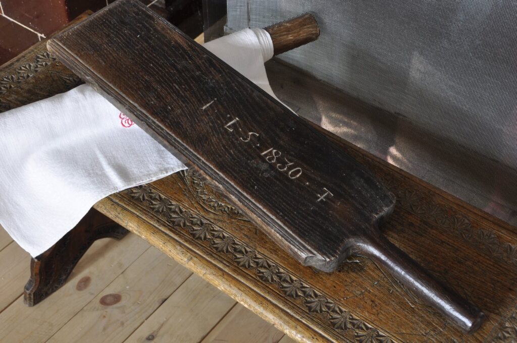 Drewniana tarkownica do prania z wyrytą datą, ułożona na ławie z białą tkaniną (kliknięcie powiększy zdjęcie).