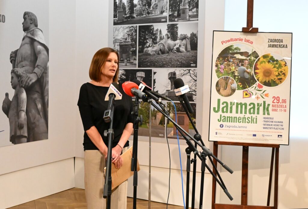 Anna Michalik opowiada o atrakcjach w Zagrodzie Jamneńskiej przygotowanych na wakacje 2025. W tle plakat reklamujący wakacyjny "Jarmark Jamneński".