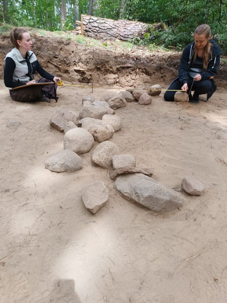 Dwie osoby robią pomiary w wykopie archeologicznym (kliknięcie spowoduje powiększenie zdjęcia).