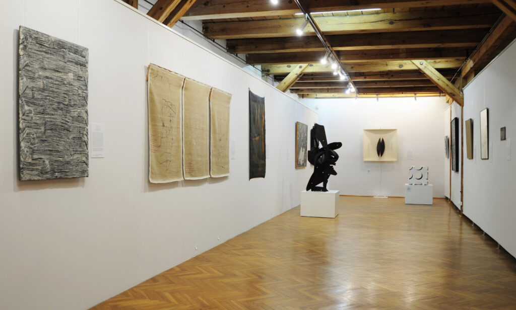 Na ściankach wystawowych wiszą prace sztuki współczesnej. W środku dwie rzeźby - kliknij aby powiększyć zdjęcie.