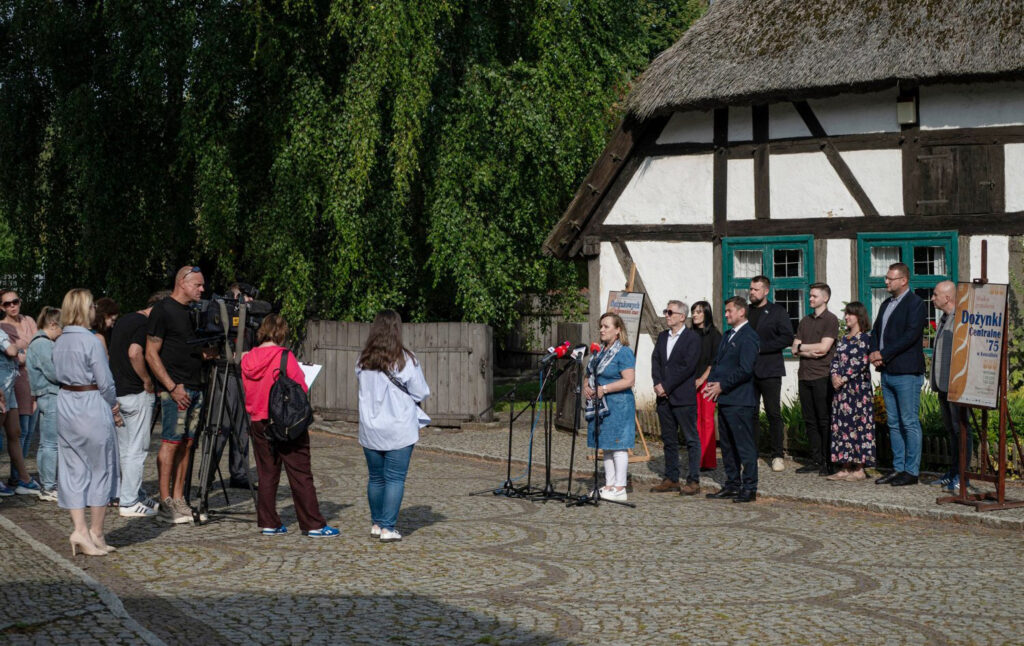 Ludzie stojący na dziedzińcu przed zabytkową chałupą rybaka. Po lewej stoją dziennikarze, a po prawej osoby wypowiadające się w konferencji prasowej (kliknięcie spowoduje powiększenie zdjęcia).