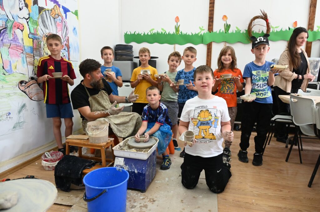 Grupowe zdjęcie dzieci. Wszystkie są obrócone przodem do kadru i pokazuję wykonane z gliny przedmioty (kliknięcie spowoduje powiększenie zdjęcia).