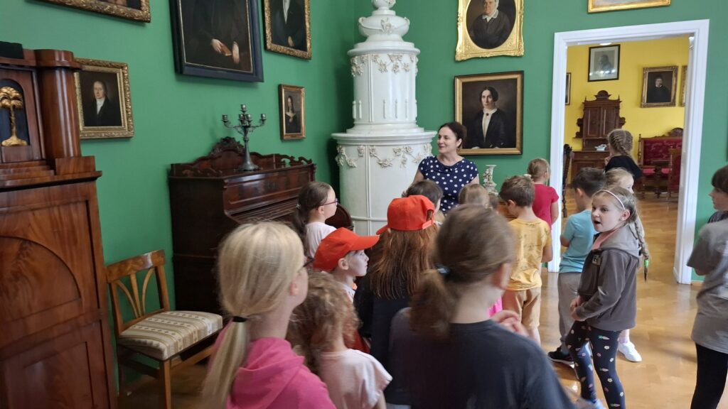 Dzieci oprowadzane są po wystawie sztuki dawnej. W pokoju wystrój w stylu biedermeier: kredensy, obrazy, stary piec (kliknięcie spowoduje powiększenie zdjęcia).