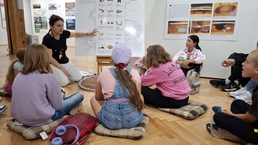 Dzieci siedzą na poduszkach, na podłodze i słuchają wykładu o gotach (kliknięcie spowoduje powiększenie zdjęcia).