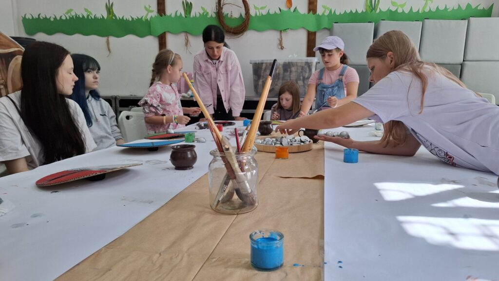 Na środku stół z narzędziami do malowania. Przy stole siedzą dzieci biorące udział w warsztatach (kliknięcie spowoduje powiększenie zdjęcia).