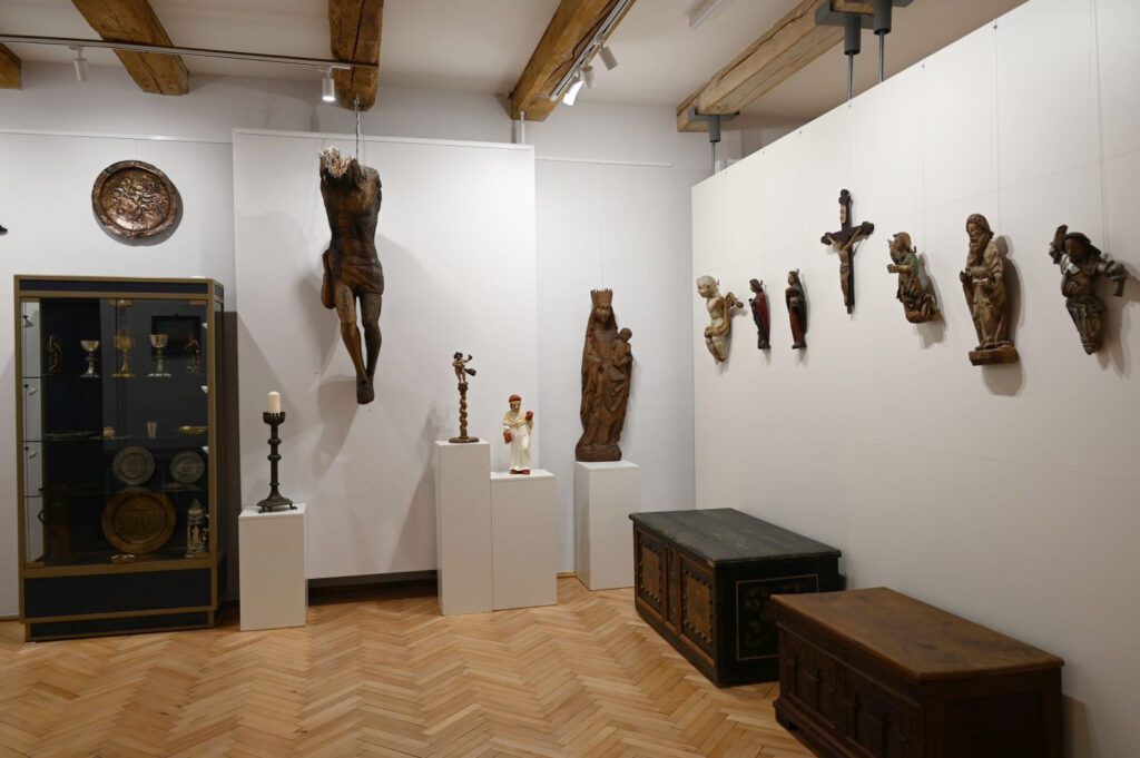 W gablocie przedmioty użytku codziennego. Na ścianach krzyże i elementy nagrobków. Po prawej stronie, pod ścianą, drewniane skrzynie (kliknięcie spowoduje powiększenie zdjęcia).