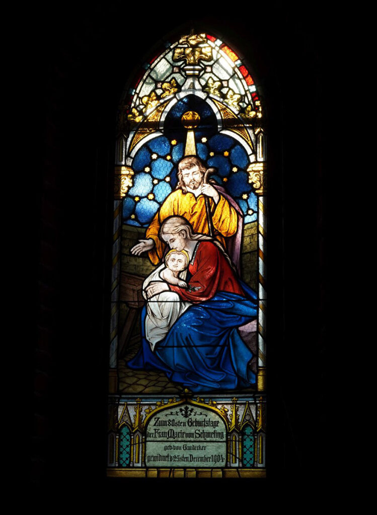 Kolorowy witraż przedstawiający Boże Narodzenie. Z tyłu stoi Józef podparty laską, a przed nim Maryja trzymająca w ramionach Dzieciątko Jezus (kliknięcie spowoduje powiększenie zdjęcia).