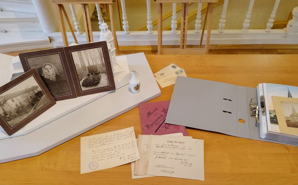 Na stole stoją trzy, czarno-białe, archiwalne fotografie. Po prawej stronie leżą archiwalne dokumenty oraz segregator (kliknięcie spowoduje powiększenie zdjęcia).