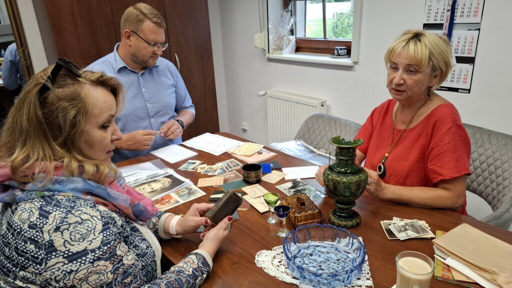 Trzy osoby siedzą przy stole - w biurze. Przeglądają zdjęcia i dokumenty przekazane do Muzeum w Koszalinie (kliknięcie spowoduje powiększenie zdjęcia).