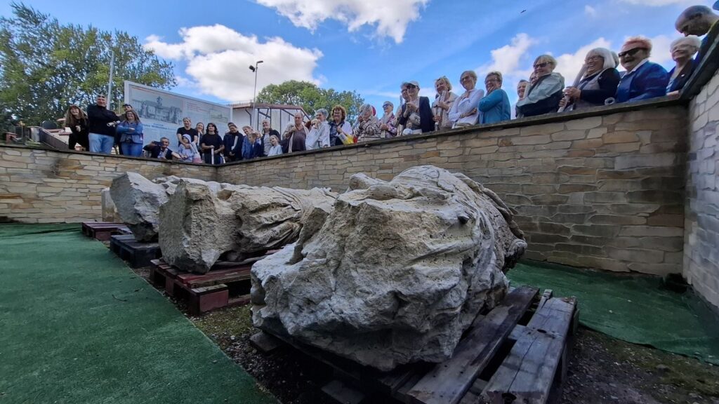 Ludzie stoją przed fosą przy budynku muzeum. W fosie znajdują się fragmenty pomnika Fryderyka Wilhelma I. W tle widoczna tablica z informacjami o pomniku (kliknięcie spowoduje powiększenie zdjęcia).