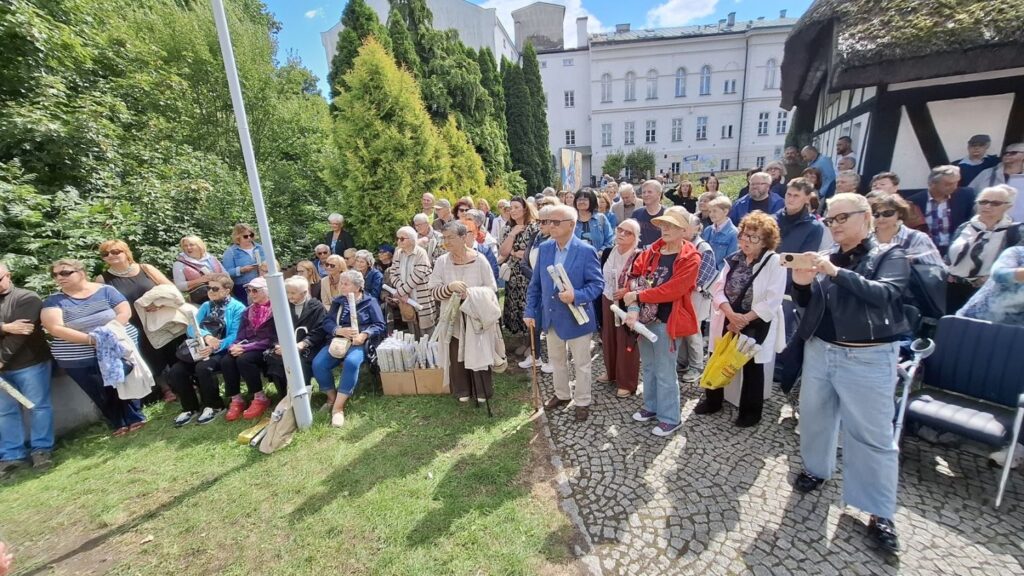 Ludzie stoją na zewnątrz, na dziedzińcu muzeum. W tle widoczny budynek muzeum (kliknięcie spowoduje powiększenie zdjęcia).