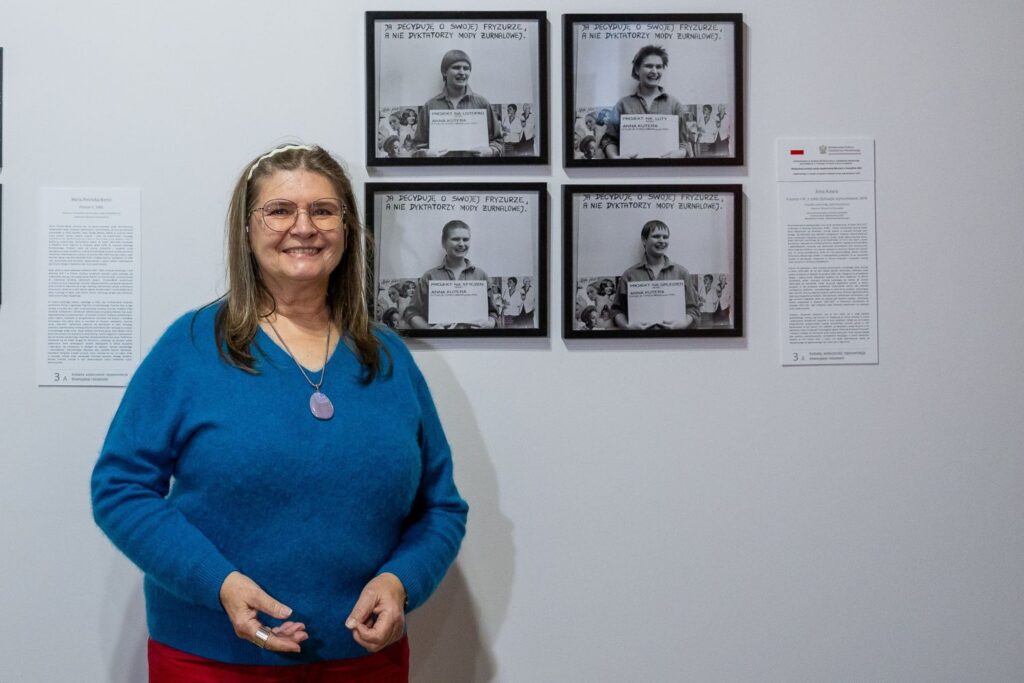 Kobieta stoi przed ścianą wystawową, na której zawieszone są cztery zdjęcia z jej podobizną z lat poprzednich (kliknięcie spowoduje powiększenie zdjęcia)