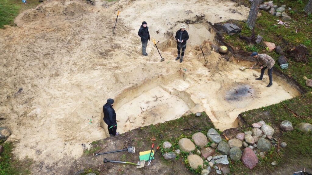 Osoby pracują w wykopie, obok którego znajdują się wykopane z ziemi kamienie i głazy (kliknięcie spowoduje powiększenie zdjęcia).