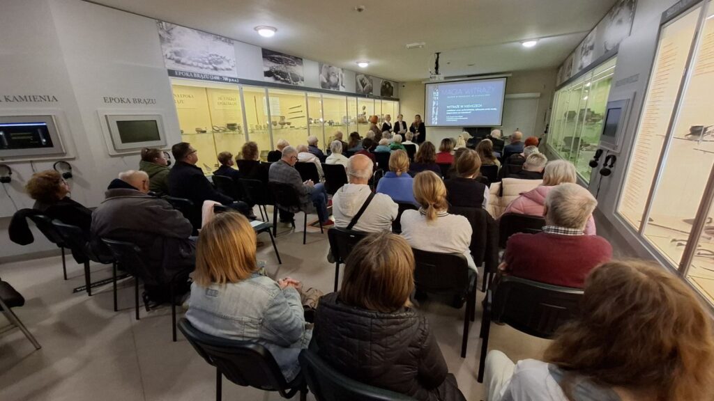 Widok sali z uczestnikami siedzącymi na krzesłach podczas prezentacji o witrażach (kliknięcie powiększy zdjęcie).