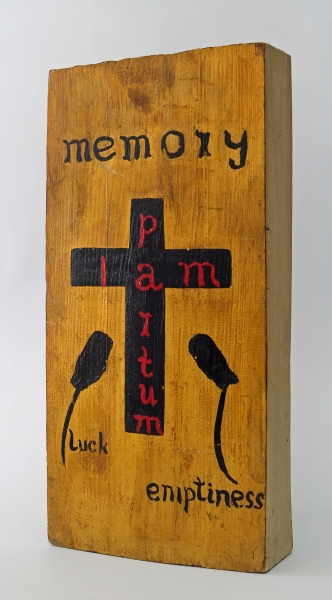 Drewniany obiekt z napisem „memory”, „partum”, „luck” i „emptiness” oraz motywem czarnego krzyża na środku (kliknięcie powiększy zdjęcie).