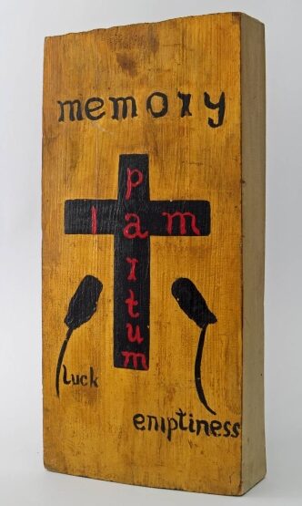 Fragment drewna w formie prostopadłościanu, na widnieją słowa: memory, luck i emptiness oraz znaki graficzne: krzyż i kwiaty (kliknięcie spowoduje powiększenie zdjęcia)