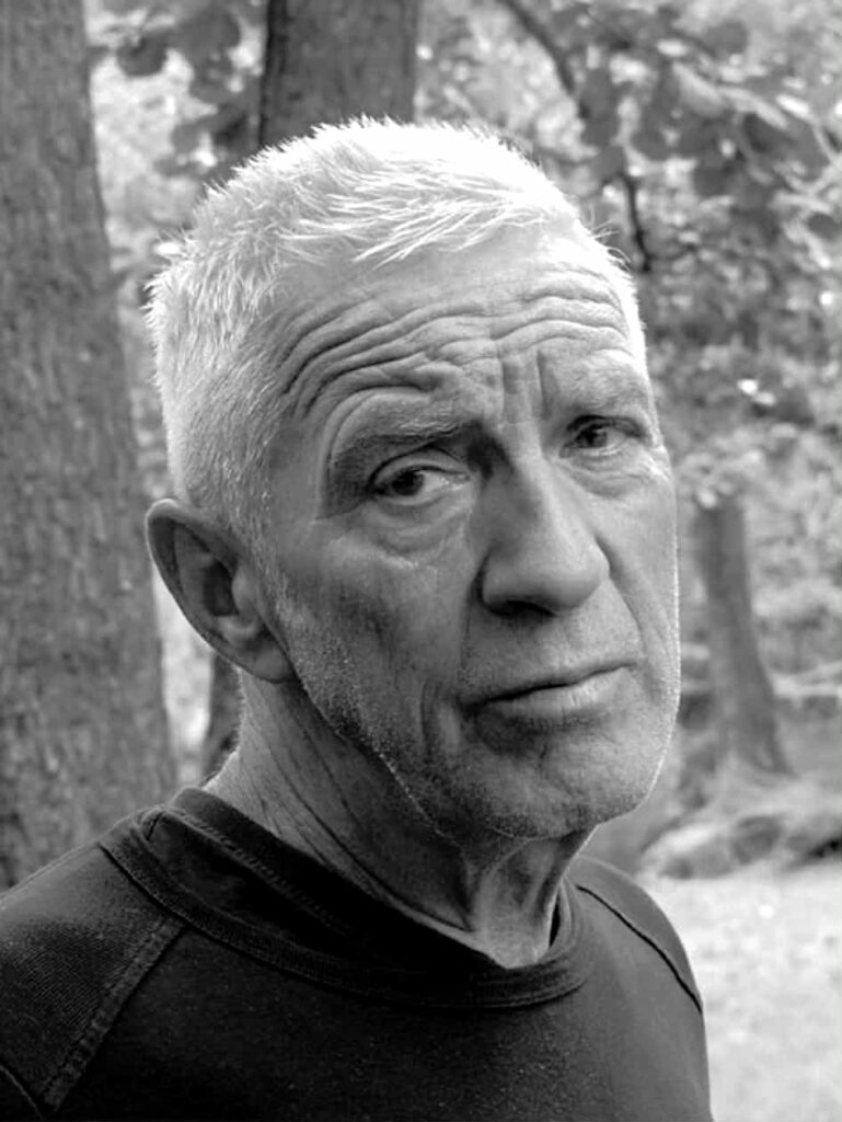 Twarz mężczyzny, który patrzy z bliskiej odległości w obiektyw. W tle drzewa i zieleń