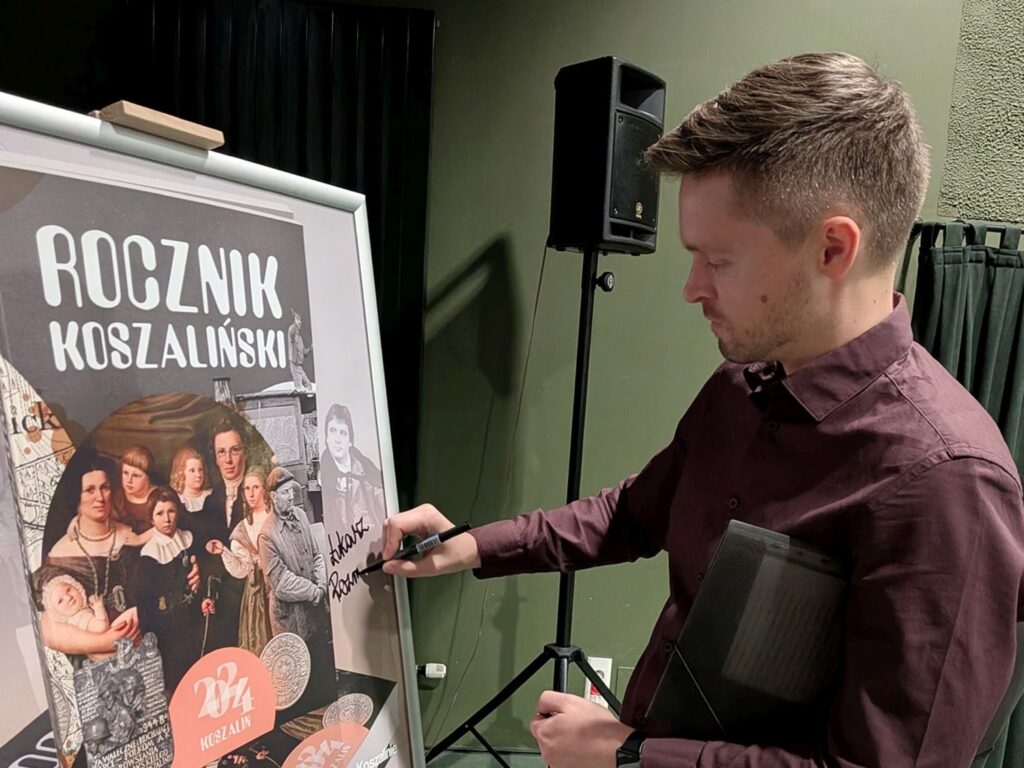 Osoba podpisuje duży plakat promujący „Rocznik Koszaliński” ustawiony na sztaludze (kliknięcie powiększy zdjęcie)