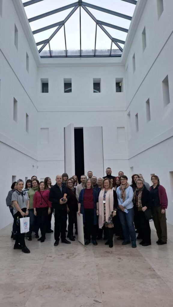 Pracownicy muzeum stoją na wysokim, jasnym atrium z przeszklonym dachem i białymi ścianami i pozują do zdjęcia (kliknięcie powiększy zdjęcie