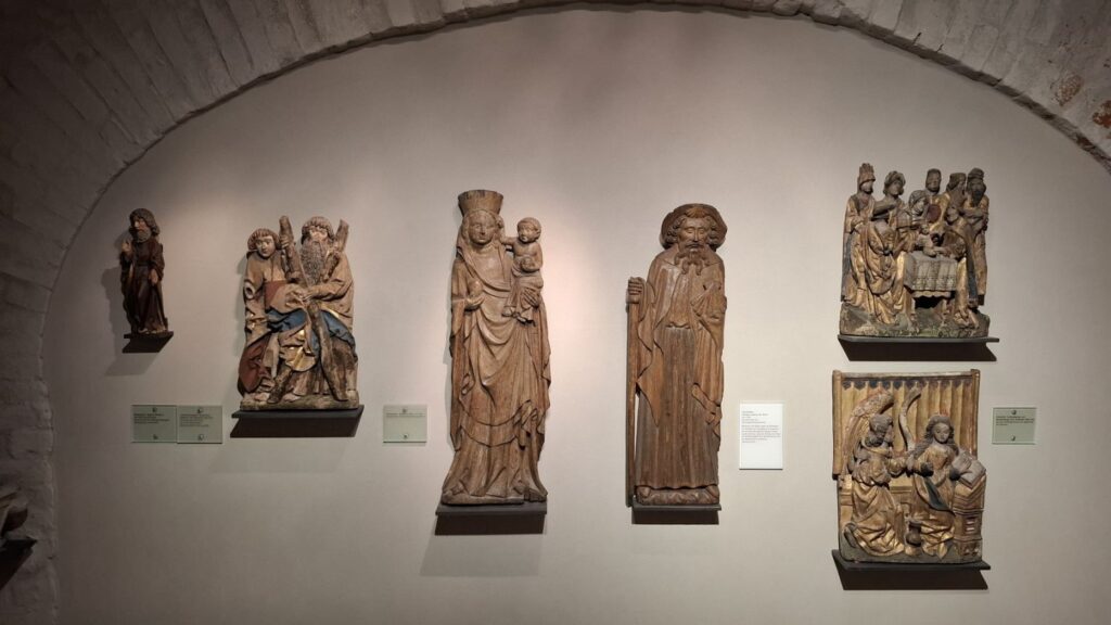 Zespół średniowiecznych rzeźb sakralnych ustawionych na ścianie w półkolistej sali muzealnej (kliknięcie powiększy zdjęcie)