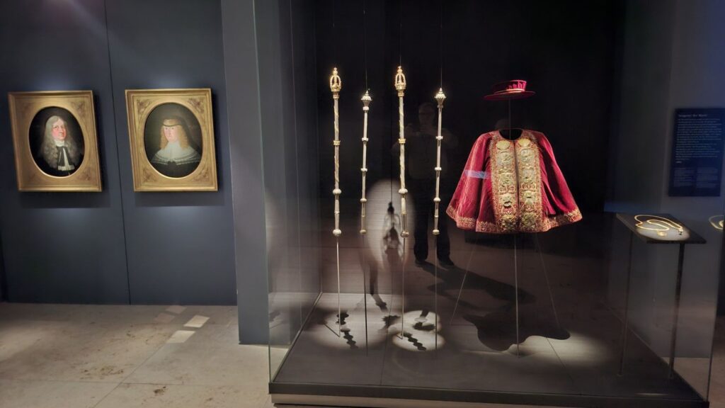 Ekspozycja muzealna z historycznymi strojami, insygniami i portretami, prezentowana w przeszklonej gablocie (kliknięcie powiększy zdjęcie)