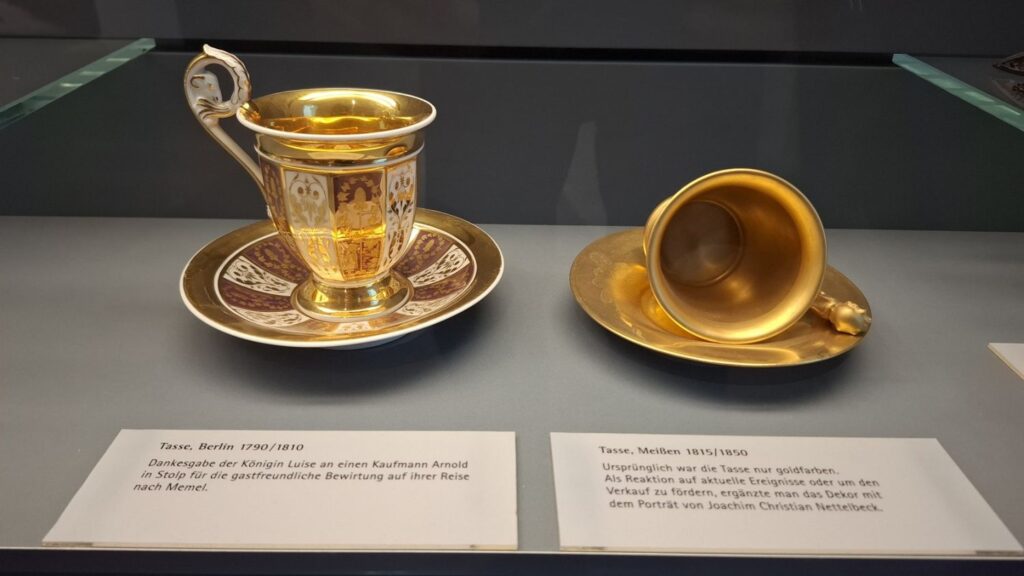 Złocona filiżanka ze spodkiem, eksponowana w muzealnej gablocie jako przykład rzemiosła artystycznego (kliknięcie powiększy zdjęcie)