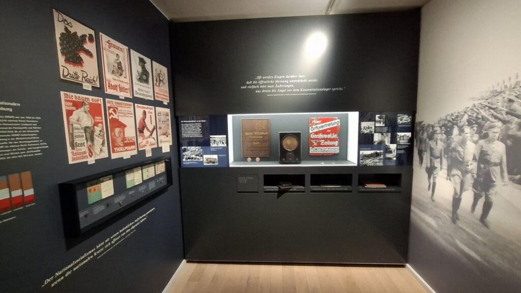 Ekspozycja muzealna z plakatami, dokumentami i fotografiami historycznymi na ciemnych ścianach (kliknięcie powiększy zdjęcie)