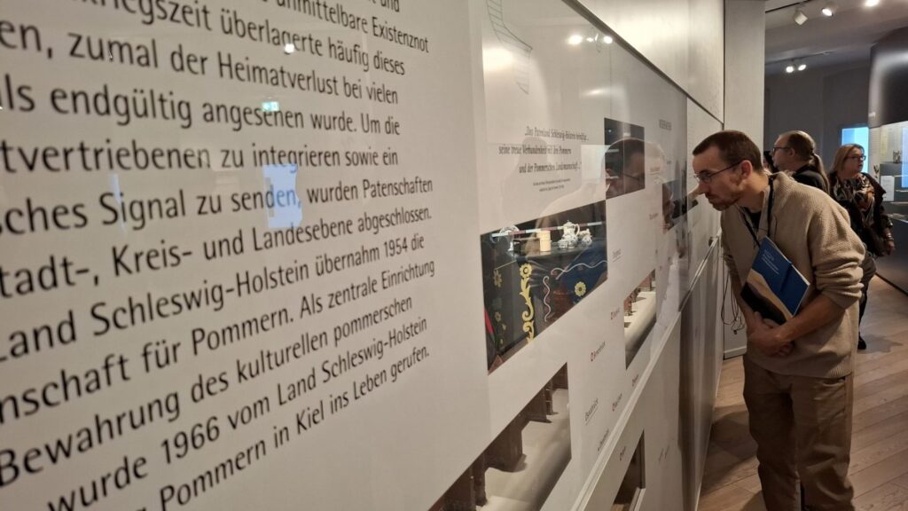 Zwiedzający czyta teksty na ścianach i ogląda eksponaty prezentowane w gablotach muzealnych (kliknięcie powiększy zdjęcie)