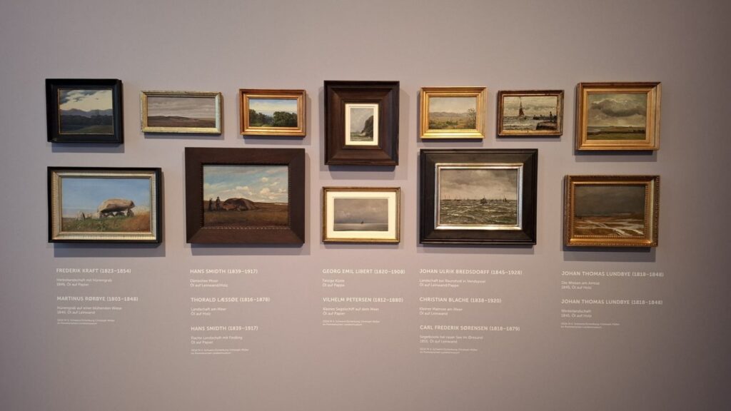 Ściana wystawy z kolekcją niewielkich obrazów pejzażowych i opisami kuratorskimi (kliknięcie powiększy zdjęcie)