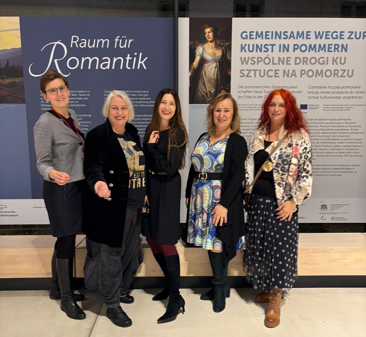 Pięć kobiet stoi przez banerem z opisem wystawy sztuki romantycznej i pozuje do zdjęcia (kliknięcie powiększy zdjęcie)